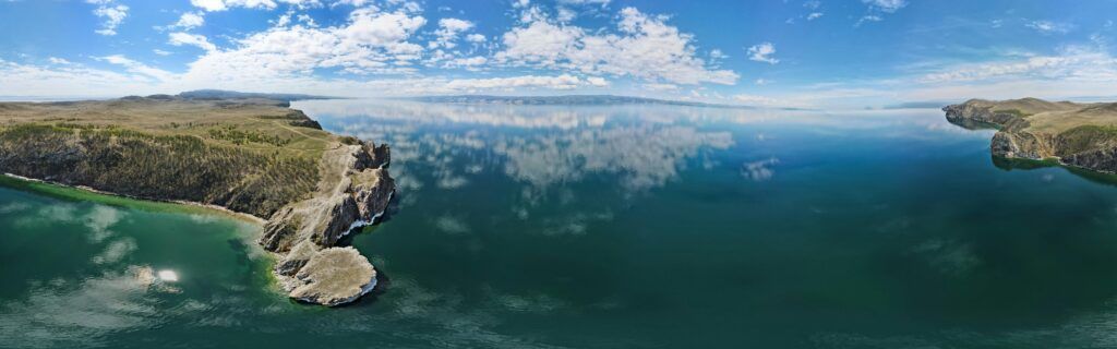A breathtaking aerial view of Lake Baikal with clear waters reflecting the sky, surrounded by rugged cliffs.
